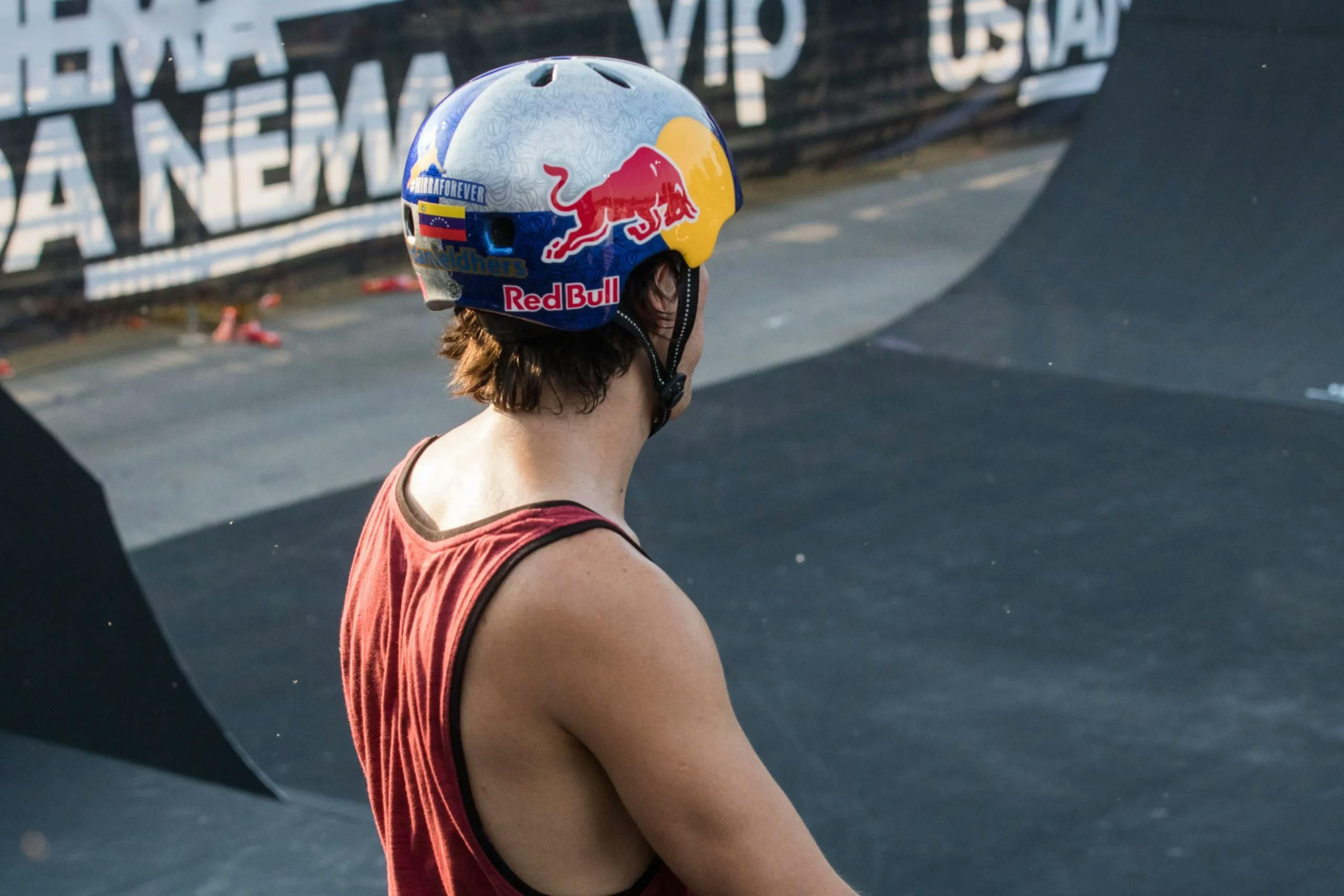 Person in a Red Bull helmet looking over a skate park ramp.